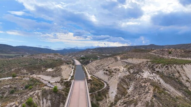 Aerial hazily drifts above an extraordinary abandoned landscape bisected by a long empty road to nowhere, deep in Almeria province Andalusia Spain. Vast skies and eroded landscapes.