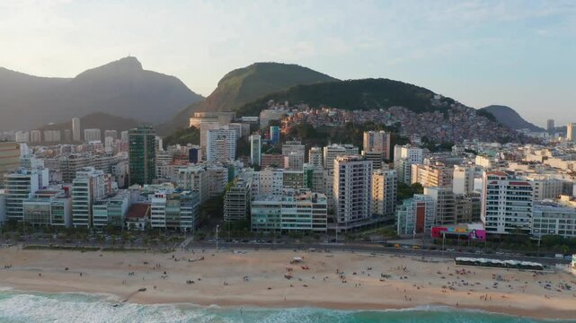 Drone shot of Ipanema Beach with buildings and the hillside of Rio de Janeiro at sunset.