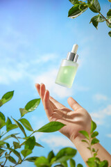 A model is seen holding a replica of a serum bottle in a shot intended to advertise the beauty product. The picture is set against a stunning blue sky with some trees and drifting clouds.