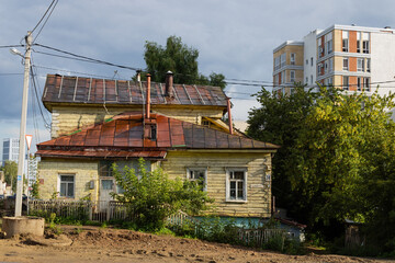 Old shabby house, dirty road. Pole and power lines. Modern high-rise buildings in the back. Eclectic architecture on the streets of Ufa. Bashkortostan