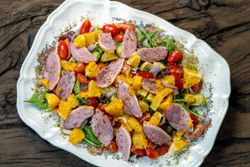 Photo of famous salad with smoked duck breast, cherry tomatoes, orange, green salad, and spices. Home cooking, restaurant. On a light background.