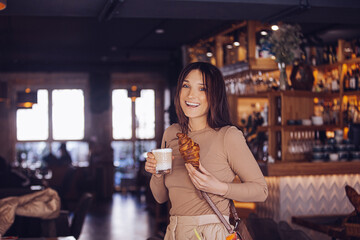 Portrait of an adult young beautiful brunette girl in a cafe with a cup of coffee and a croissant