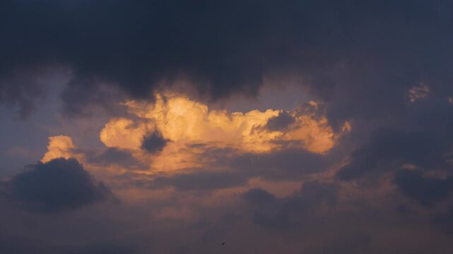 Sunset emitting orange sunrays making the cloud orange colored inside dark clouds.