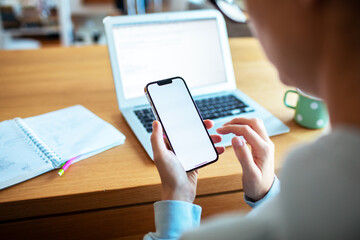 Woman checking blank smartphone screen while working on laptop at home