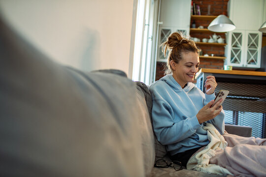 Young adult woman using smartphone on the sofa at home