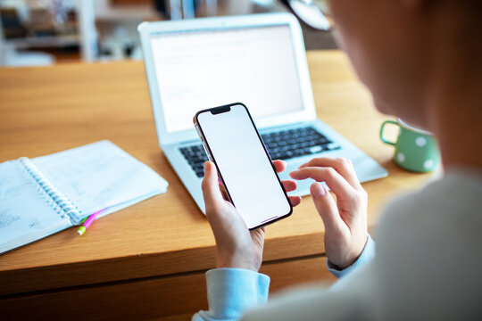 Woman checking blank smartphone screen while working on laptop at home