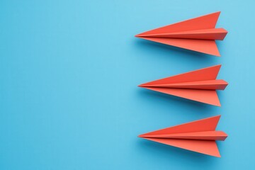 Fototapeta premium Three red paper airplanes on a blue background, symbolizing creativity, imagination, and flight.