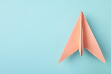 A minimalist image of a folded peach paper airplane on a soft blue background, evoking creativity and playfulness.