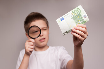 the boy examines a bill of hundred euro through the magnifying glass