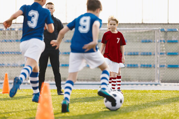 Fototapeta premium Group of boys attending soccer football training on a school grass pitch. Man coaching children in physical education class. Soccer practice for teenage boys. Soccer players in red and blue uniforms