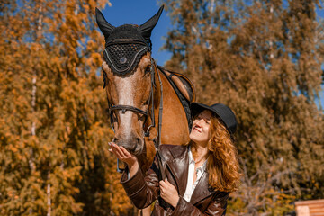 Stylish professional female jockey standing near horse. Friendship with horse. 