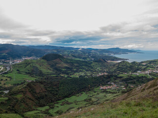 Naklejka premium Panoramic view of rolling green hills, coastal villages, and distant mountains under a cloudy sky near the sea