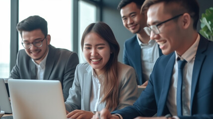 Four diverse young business professionals collaborating on laptops and smiling in a modern office setting
