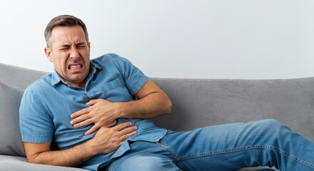 Fototapeta premium Man Gripping His Stomach in Pain While Sitting on a Couch