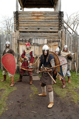 Group of medieval warriors equipped with shields and swords standing in front of a wooden fortress...