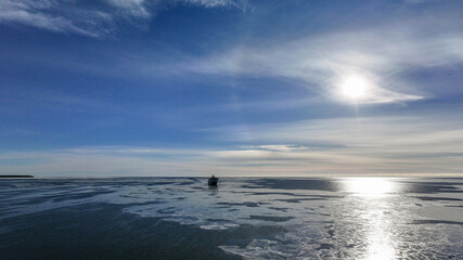 Naklejka premium Cargo Ship Far Away in the Horizon on a Bright, Sunny, Clear Winter Day on a Calm, Dark Blue Semi-Frozen Sea