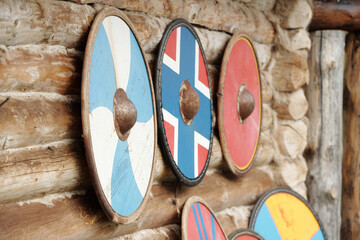 Several Viking shields are hanging on a rustic wooden wall. Each shield displays unique designs,...