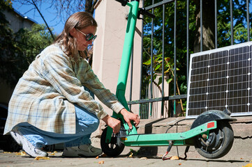 Woman connecting solar panel to electric scooter, highlighting practical application of sustainable...