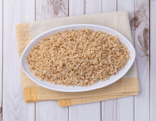 Cooked brown whole rice in a plate over wooden table