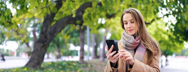 Young woman walking in a park with smartphone in her hands. Speaking on phone or sending messages...
