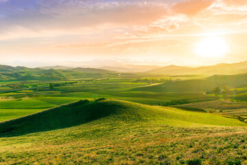 Fototapeta premium beautiful green valley with green fields with green spring grass with nive hills and mountains and scrnic colorful cloudy sunset on background of landscape