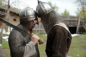 Historic reenactment showing two medieval knights in chainmail armor and helmets facing each other...