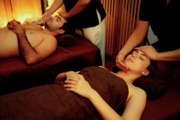 Obraz premium Couple customer enjoying relaxing anti-stress head massage and pampering facial beauty skin recreation leisure in warm candle lighting ambient salon spa in luxury resort or hotel. Quiescent
