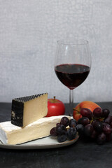 Glass of red wine with cheese, grapes and apples on grey background with copy pace. 