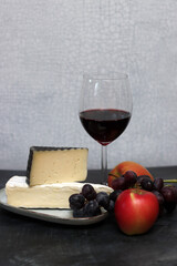 Glass of red wine with cheese, grapes and apples on grey background with copy pace. 