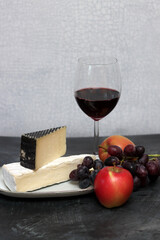 Glass of red wine with cheese, grapes and apples on grey background with copy pace. 