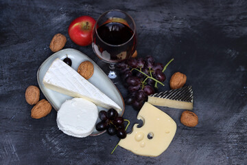 Glass of red wine with cheese, grapes and apples on grey background with copy pace. 