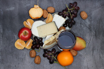 Glass of red wine with cheese, grapes and apples on grey background with copy pace. 