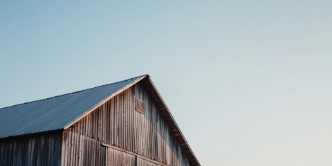 Fototapeta premium A minimalist shot of a rustic wooden barn with a metal roof, set against a bright, clear sky. The simplicity highlights the rural charm and peaceful atmosphere. 
