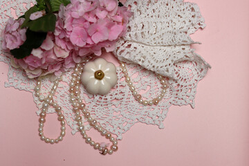 White lace, pearls and pink hydrangea on pink background with space for text
