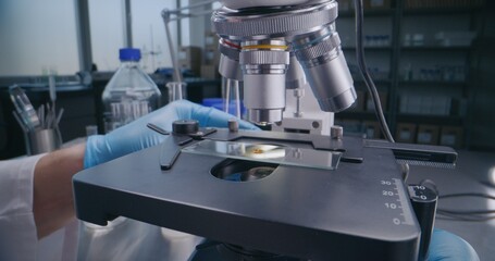 Medical science laboratory: Close up of professional microbiologist or scientist in gloves putting glass slide with test sample under microscope for analysis, developing drugs. High-tech lab device.