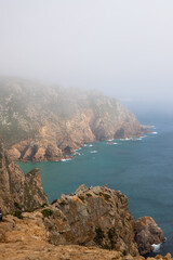 A dramatic coastal scene with rugged cliffs, crashing waves, and a lighthouse shrouded in mist. Perfect for projects related to travel, nature, or adventure.