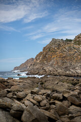 A rugged coastline with dramatic cliffs and crashing waves. The image showcases a rocky landscape, with large boulders scattered along the shore.