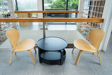 Modern seating area featuring two light wooden chairs and a round black table, creating a cozy space in a bright, minimalist interior.
