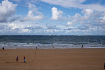 A beautiful sunny day on the beach with clouds and some people wandering