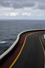 Winding road by the ocean, dramatic cliffs, stormy sky.