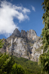 A breathtaking panorama of a majestic mountain range, with a dramatic cloud formation casting a shadow over the rugged peaks. Lush greenery covers the lower slopes, contrasting with the stark, rocky c