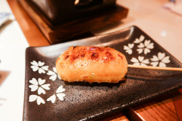 close up of Japanese smashed octopus cuttlefish paste skewer kushiyaki on a black plate with white flower pattern