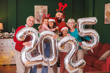 Family holding giant balloons shaped as numbers 2025 while celebrating New Year at home