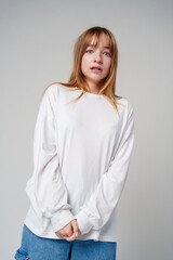 A young woman with light brown hair and blue eyes expresses surprise in a minimalist studio