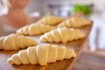 Unbaked raw croissants on wooden board, prepared for oven, held in woman’s hands, showcasing...