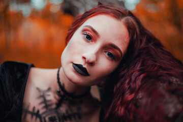 Charming red-haired witch in an autumn forest with a magical atmosphere, Halloween