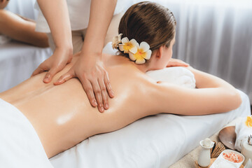 Caucasian couple customer enjoying relaxing anti-stress spa massage and pampering with beauty skin recreation leisure in day light ambient salon spa at luxury resort or hotel. Quiescent