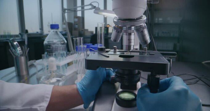 Medical science lab: Close up of professional microbiologist or scientist in gloves setting up microscope for analysis, developing vaccine. Glass slide with test sample. High-tech laboratory equipment