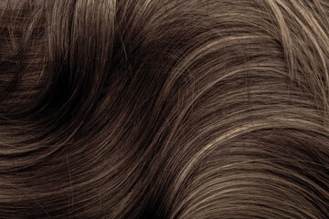 Brown hair close-up as a background. Women's long brown hair. Beautifully styled wavy shiny curls. Hair coloring. Hairdressing procedures, extension.