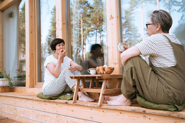 Two sisters senior women enjoying coffee on wooden patio